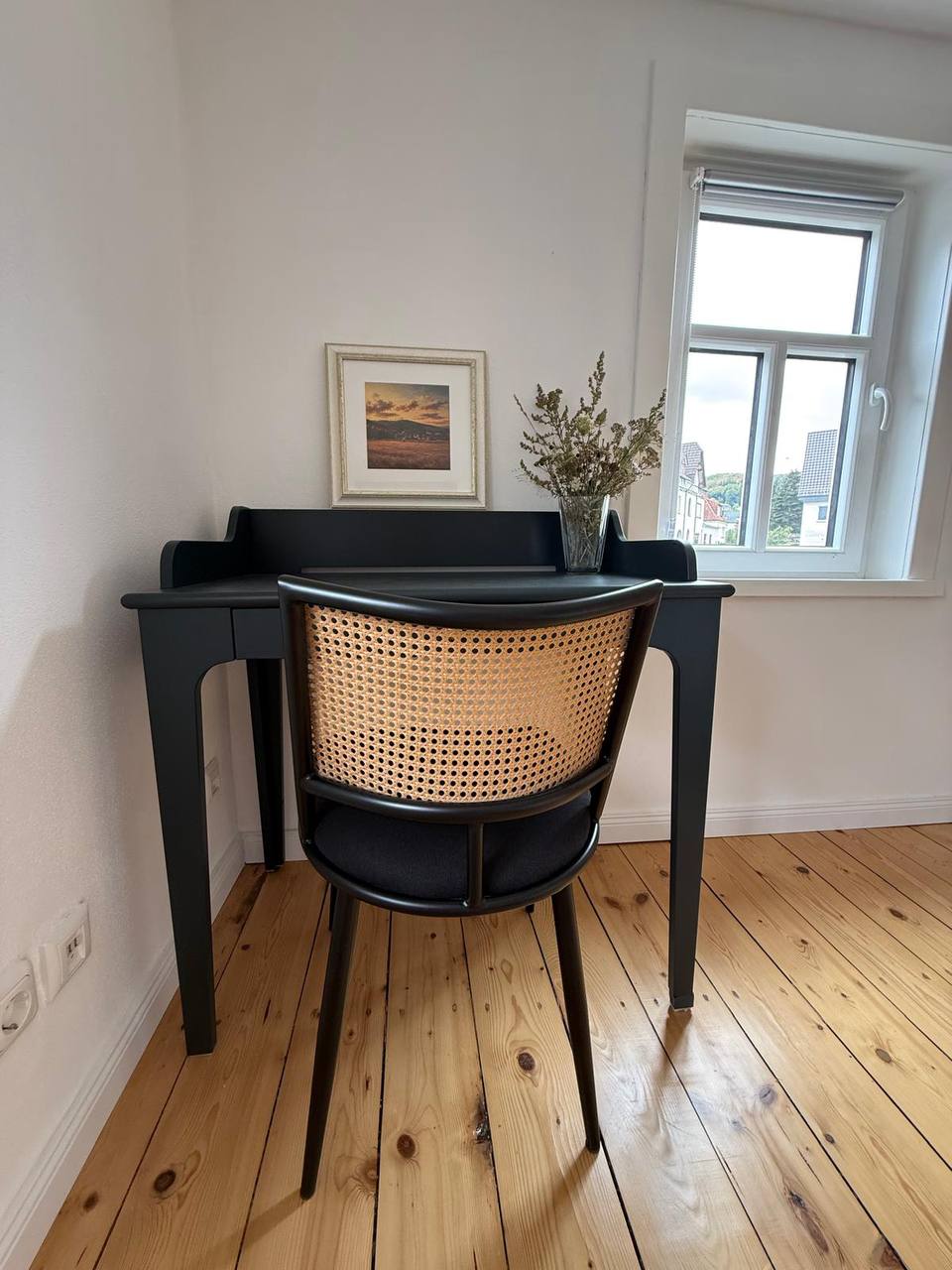 Arbeitsplatz mit schwarzem Schreibtisch und Rattanstuhl